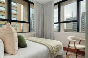 A hotel room with a large bed, a chair, and a view of the city through large windows. - Charlie and the Chairman | 2 Bedroom City Escape (Cape Town)
