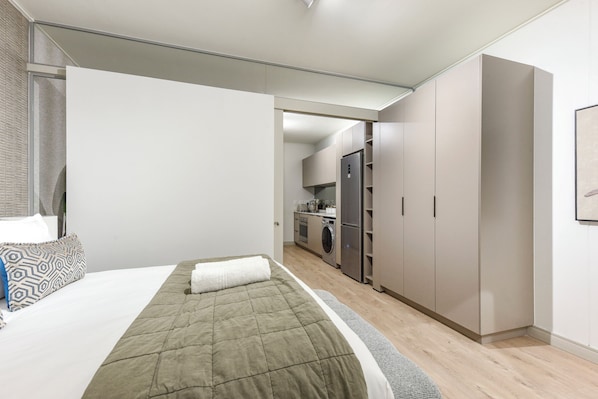 Ein modernes Schlafzimmer mit einem Bett, einem Kleiderschrank und einer kleinen Küchenzeile im Hintergrund.