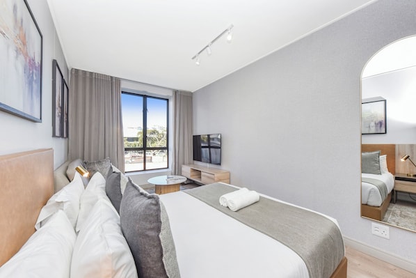 Ein modernes Hotelzimmer mit einem großen Bett, einem Fernseher, einer Sitzecke mit Tisch und einem Balkon mit Blick.