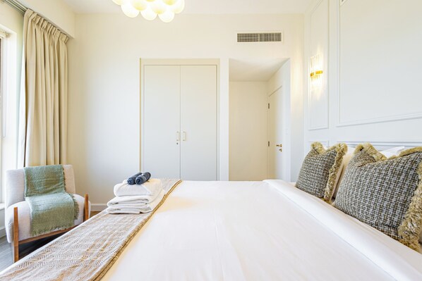 A hotel room with a large bed, a chair, a bedside table, and a wardrobe. - Upgraded Modern 3BR+Kids | JBR | Sea and Ain View (Dubai)