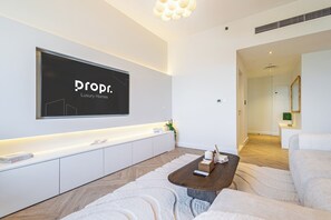 Un salon moderne avec un téléviseur à écran plat fixé au mur, une console blanche, une table basse en bois et un grand canapé blanc.