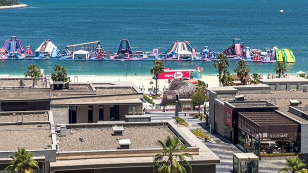 A beachside view with colorful water slides, a beach, and a building with a sign that reads 'aqua fun'. - Upgraded Modern 3BR+Kids | JBR | Sea and Ain View (Dubai)