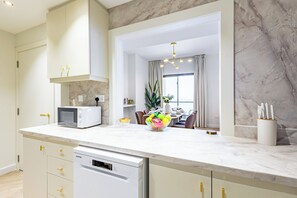 A modern kitchen with a built-in microwave, a dishwasher, and a dining area with a table set for two. - Upgraded Modern 3BR+Kids | JBR | Sea and Ain View (Dubai)