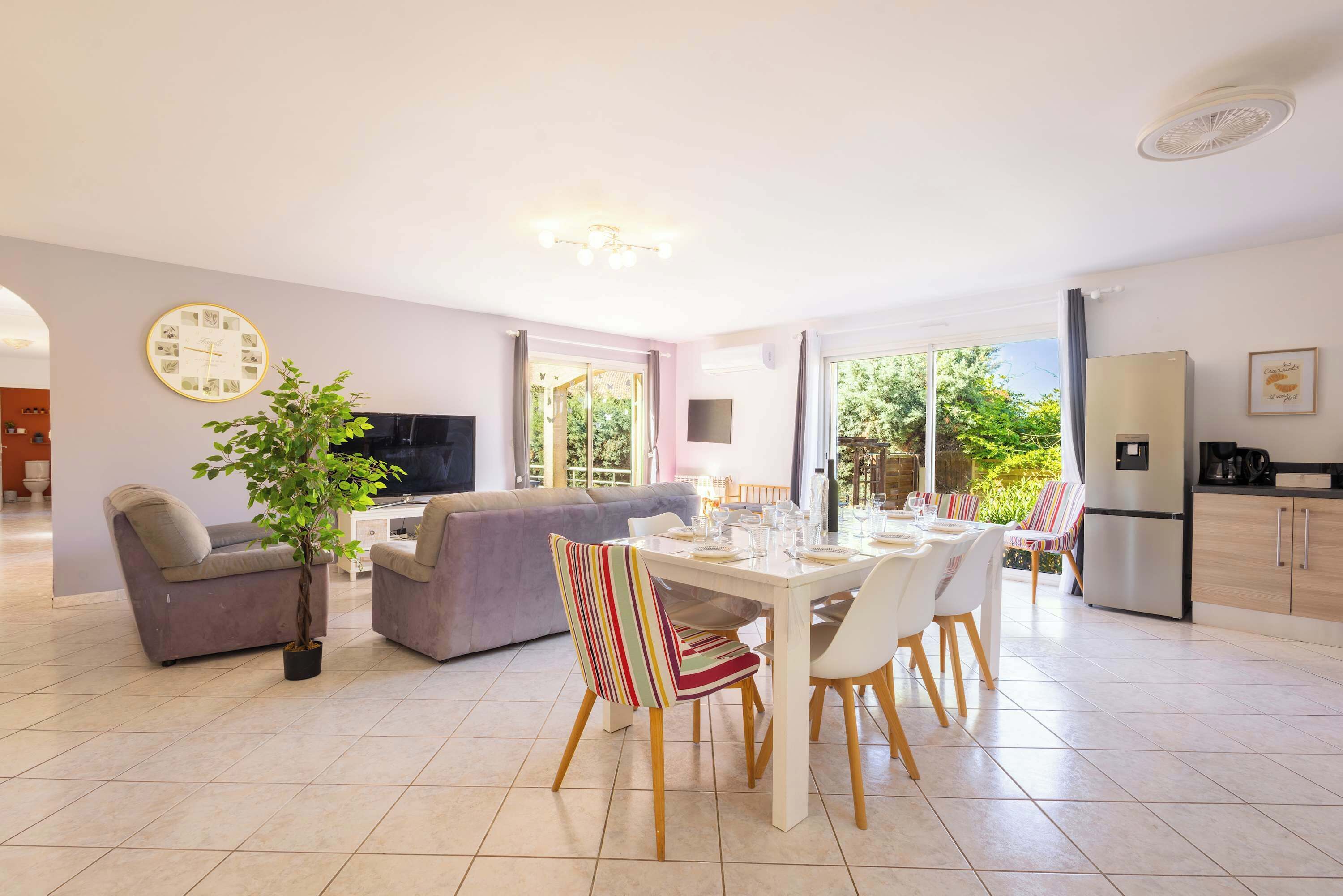 A modern living room with a sofa, a dining table set for four, and a kitchen area with a refrigerator.