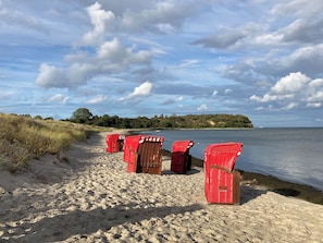 Ein Strand mit roten Liegestühlen, die am Sand aufgereiht sind, ruhige See und eine entfernte, bewaldete Insel.