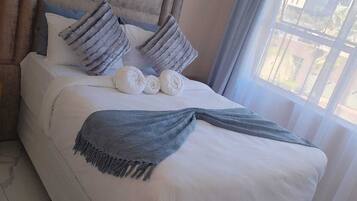 A neatly made bed with pillows and a blanket, a headboard, and a window with curtains.