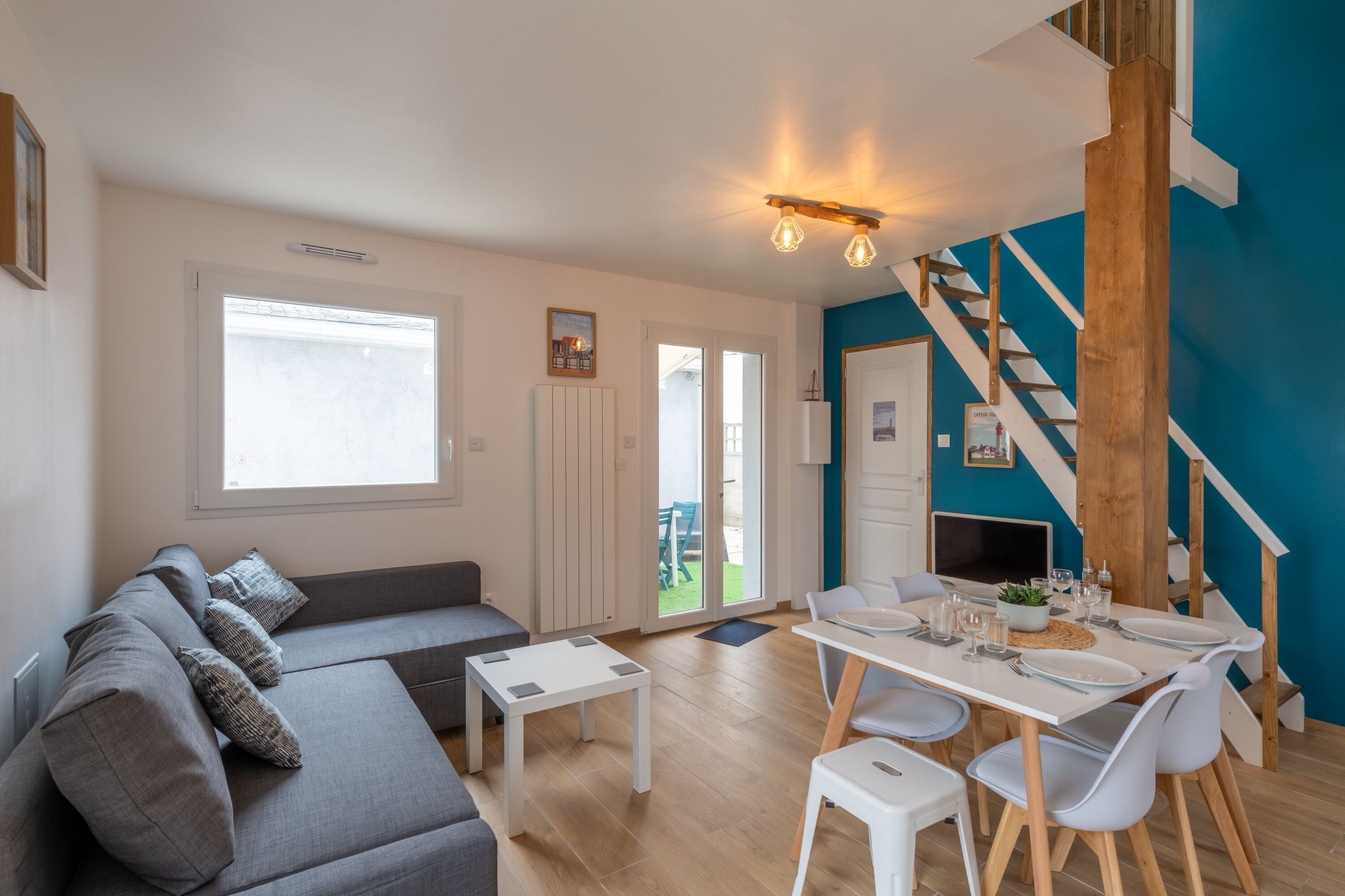 Ein zeitgemäßer Wohnraum mit grauem Sofa, einem Esstisch mit Stühlen, einer Treppe und Blick ins Freie.
