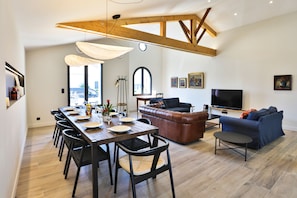 A modern living room with a dining area, a leather sofa, a TV, and a large window. - Villa les Capucines - Climatisée avec piscine (Saint-Hilaire-de-Riez)