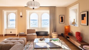 A modern living room with a sofa, a glass coffee table, and a view of the sea through large windows.