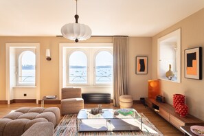 Una sala moderna con sofá, una mesa de centro de vidrio y vista al mar a través de ventanas amplias.