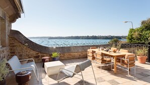 A terrace with a view of boats on the water, a table with chairs, and potted plants.