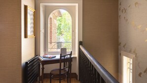 A room with a wooden desk, a chair, a window with an arch, and a staircase railing.
