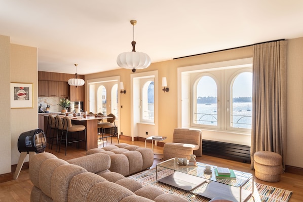 A modern living room with a sofa, a coffee table, and a view of the sea through large windows.