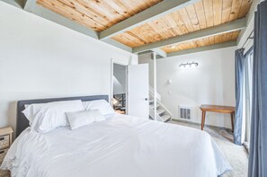 Une chambre à coucher avec un lit, un plafond en bois, un escalier et une fenêtre avec des rideaux.