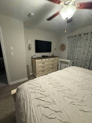 Een slaapkamer met een bed, een dressoir, een televisie en gordijnen met een patroon.