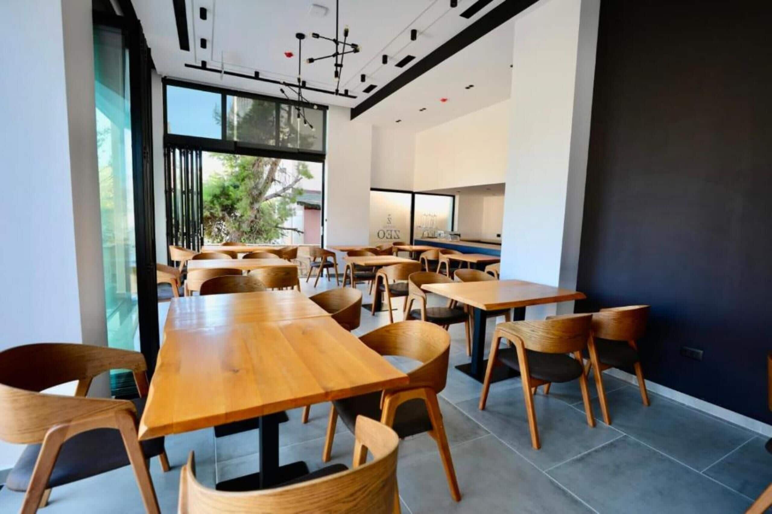 Uma sala de jantar moderna com mesas e cadeiras de madeira, janelas amplas e vista para o verde lá fora.