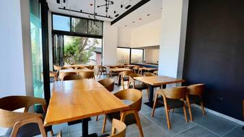 Uma sala de jantar moderna com mesas e cadeiras de madeira, janelas amplas e vista para o verde lá fora.