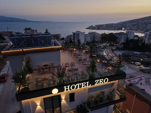 Un hotel llamado HOTEL ZEO con una terraza en la azotea que ofrece asientos al aire libre y vistas a la ciudad y al mar.