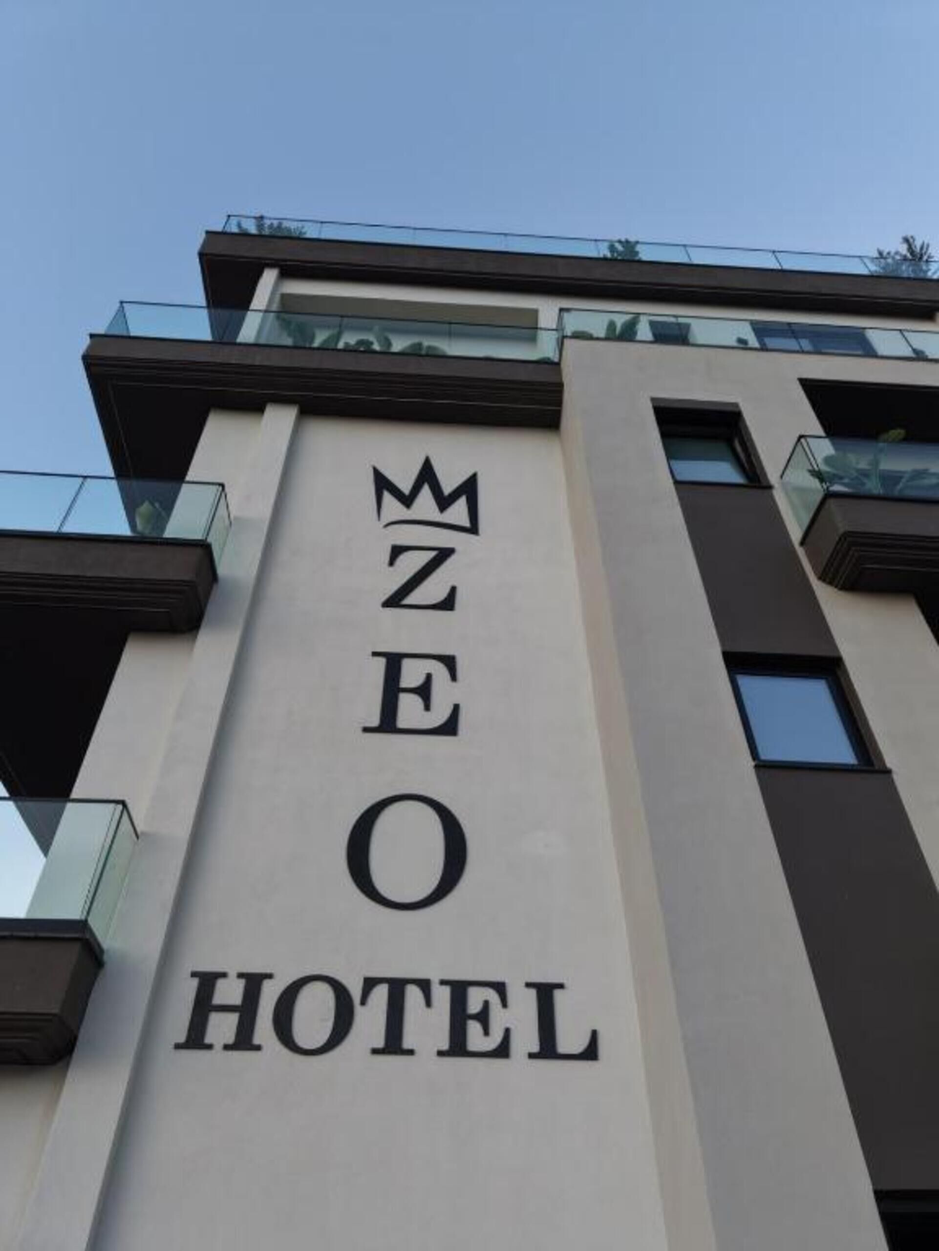 Placa de hotel com o nome 'ZEO HOTEL' e um símbolo de coroa acima do 'E'.