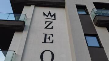 Placa de hotel com o nome 'ZEO HOTEL' e um símbolo de coroa acima do 'E'.