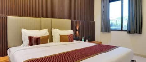 A hotel room with a large bed, a wooden headboard, a nightstand, and a window with curtains.