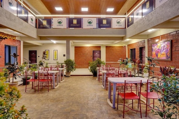 Un vestíbulo de hotel con varias zonas de estar, plantas en macetas y una escalera central.