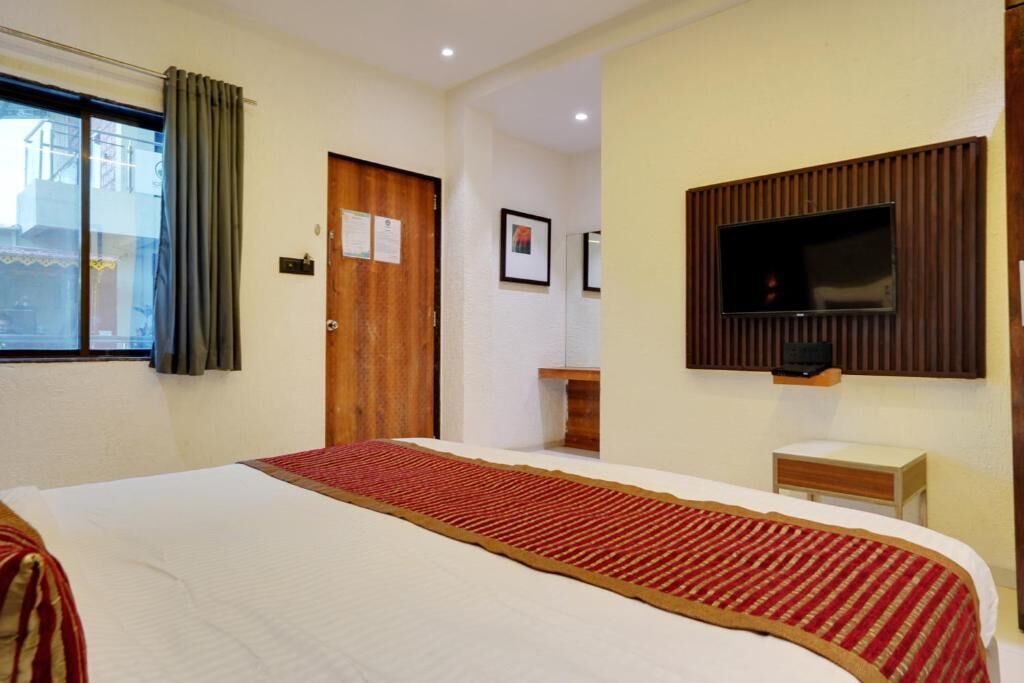 Habitación de hotel con una cama grande, un televisor montado en la pared y una ventana con cortinas.