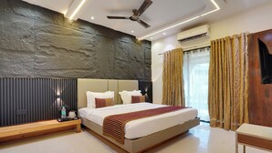 A modern hotel room with a large bed, a wooden bench, a ceiling fan, and an air conditioning unit. - Hotel Iceberg Mahabaleshwar Venna Lake  (Mahabaleshwar)