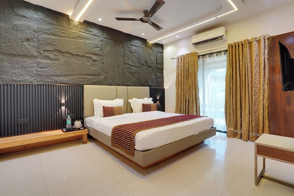 Quarto de hotel moderno com uma cama grande, um banco de madeira, um ventilador de teto e um aparelho de ar condicionado.