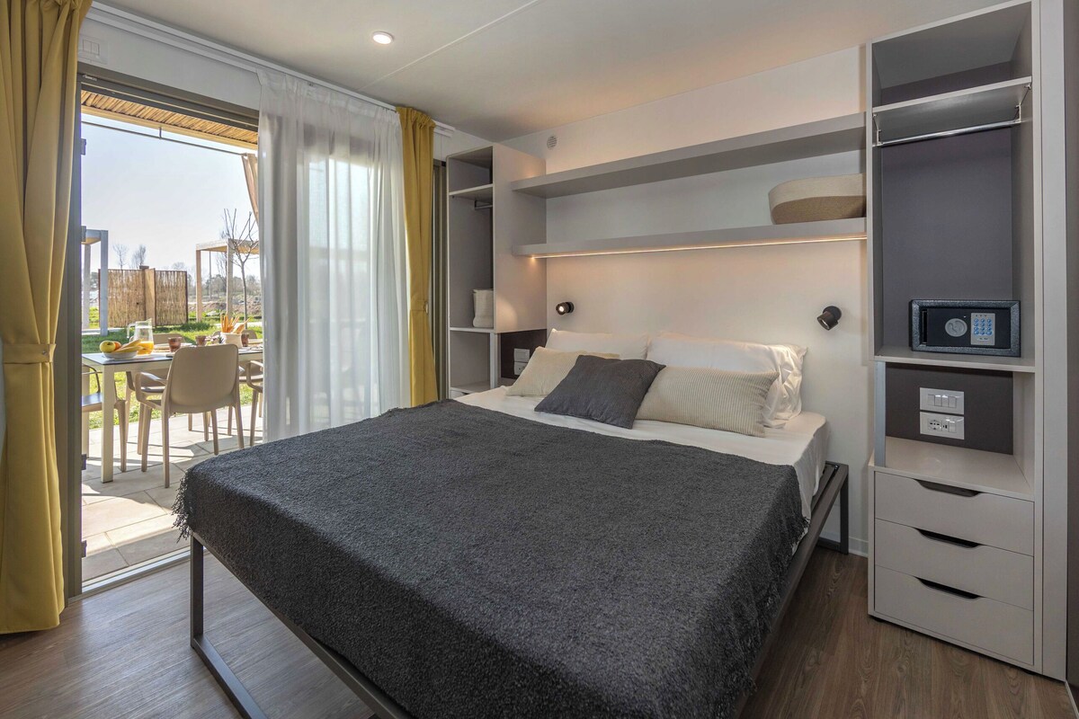 A modern bedroom with a bed, bedside tables, a built-in wardrobe, and a view of the outdoors.
