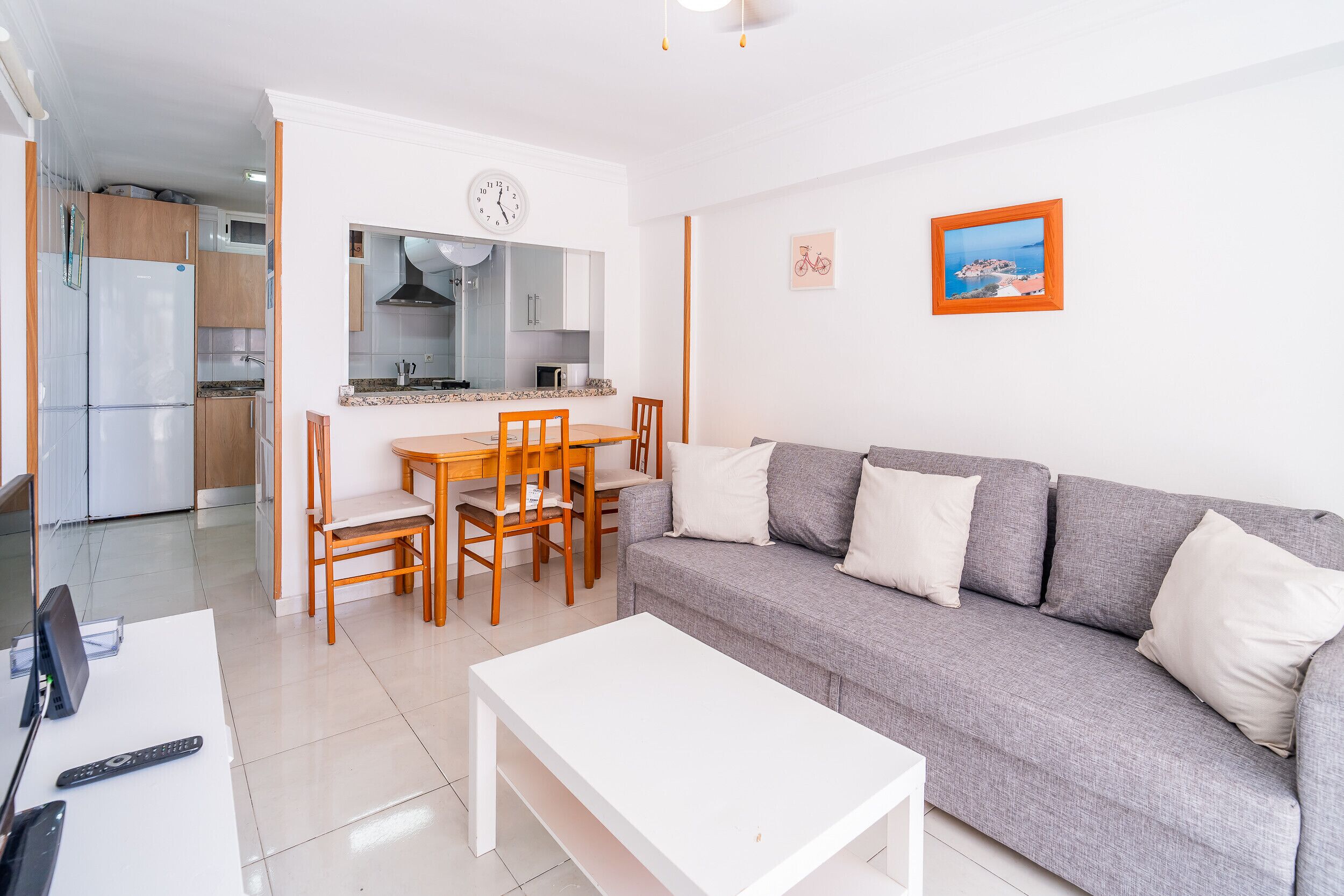 A modern living room with a grey sofa, a white coffee table, and a dining area with wooden chairs and a table.