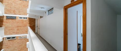 A narrow balcony with a white railing, a door with a wooden frame, and a trash bin.