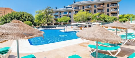 A swimming pool with lounge chairs and umbrellas, surrounded by a building with multiple balconies.