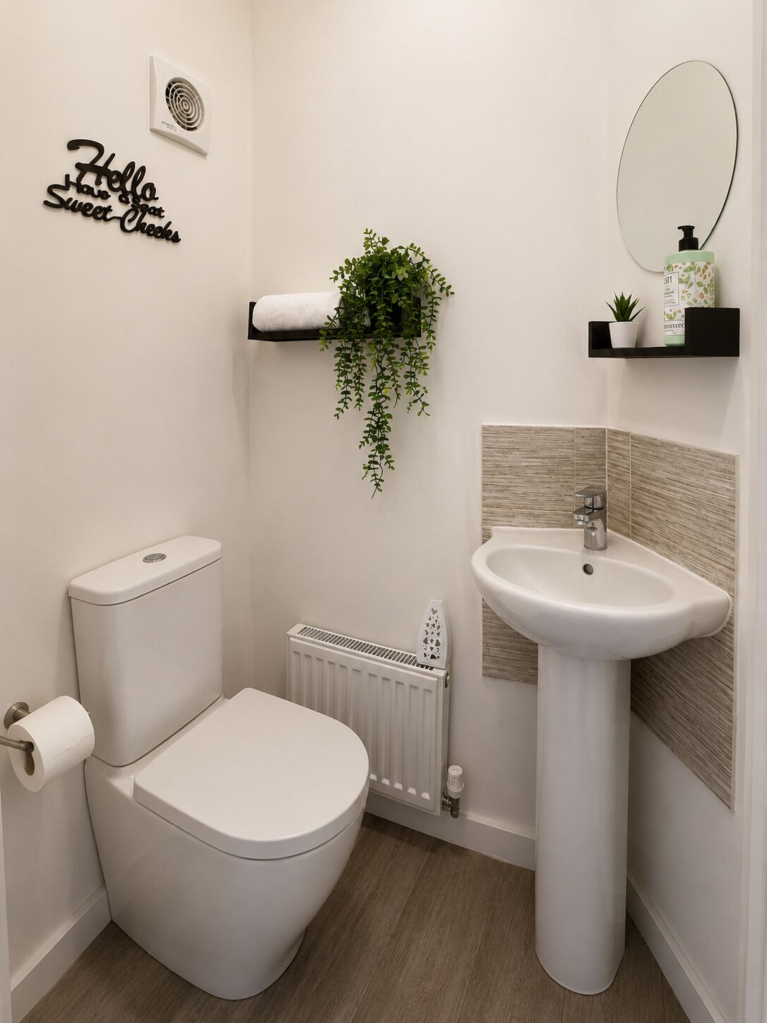 Een moderne badkamer met toilet, wastafel, spiegel, handdoekradiator en een wandplant.