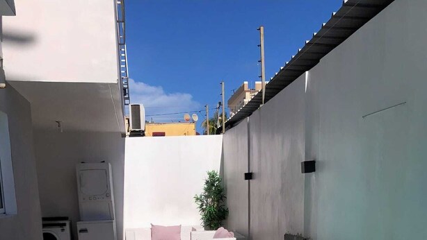 Una piscina con suelo de baldosas, una pared blanca y un pequeño rincón de descanso con cojines.
