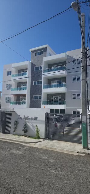 A multi-story residential building with balconies, a gated entrance, and a clear sky. - Apartment in Arismar (Santo Domingo Este)