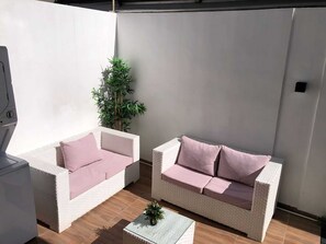 A patio area with two white wicker sofas, each with a single pink cushion, and a small table with a potted plant. - Apartment in Arismar (Santo Domingo Este)