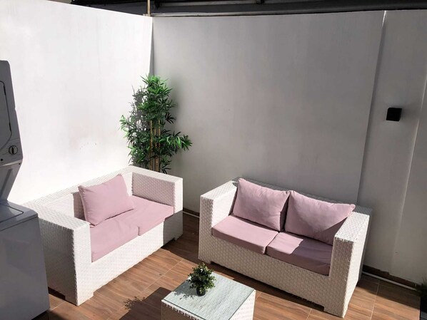 Ein Patio mit zwei weißen Korbuscheln, jeweils mit einem einzelnen rosafarbenen Kissen, und einem kleinen Tisch mit einem Blumentopf.