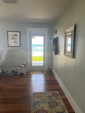 A hallway with a door leading to a beach view, a framed fish picture, a woven basket with clothes, and a patterned rug. - Beautiful custom home on the beach (Ormond Beach)