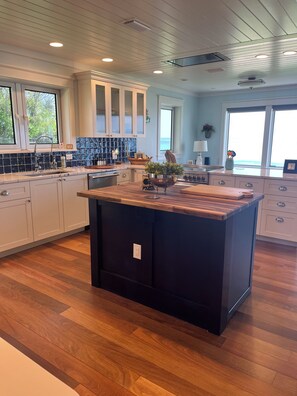 A modern kitchen with a central island, wooden flooring, and a view of the ocean through large windows. - Beautiful custom home on the beach (Ormond Beach)