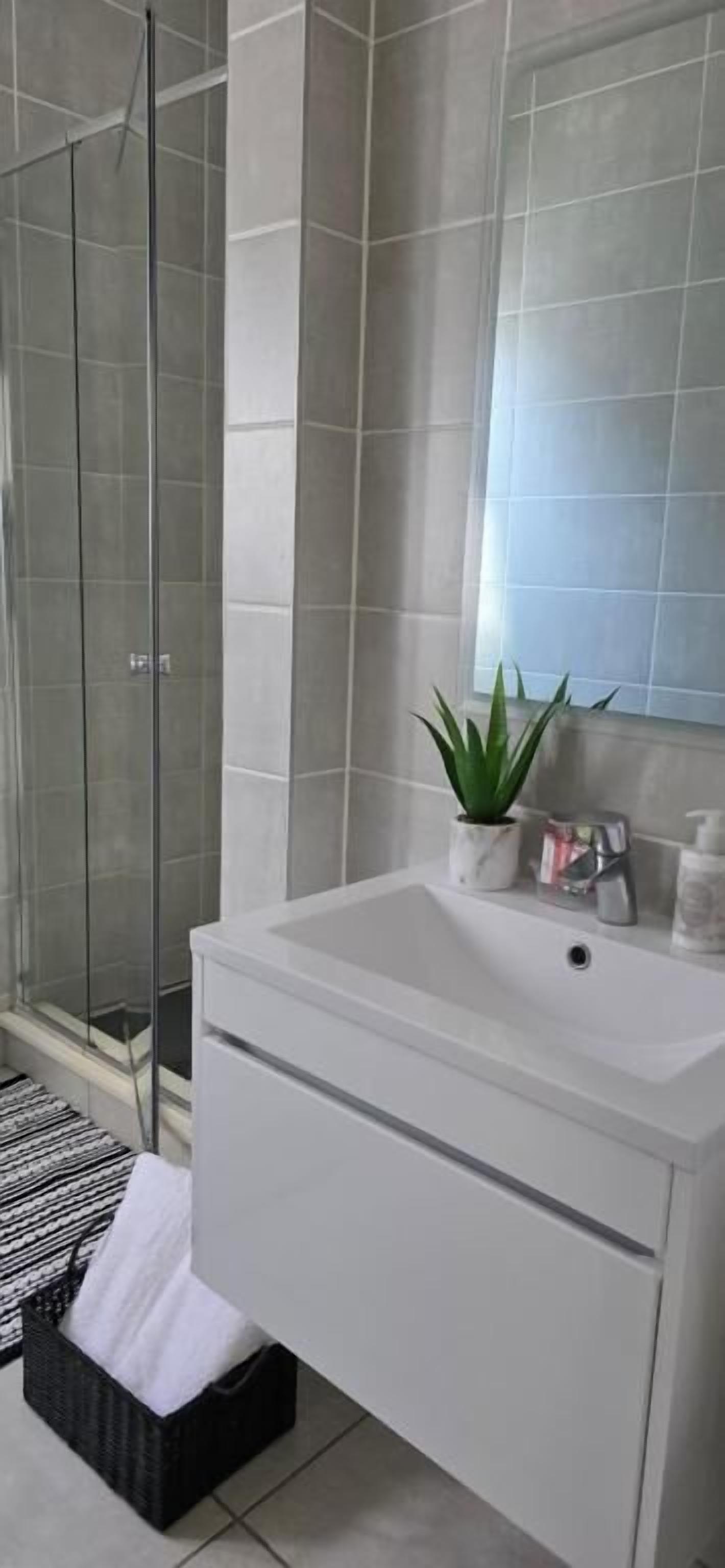 A modern bathroom with a glass shower enclosure, a white sink, and a mirror.