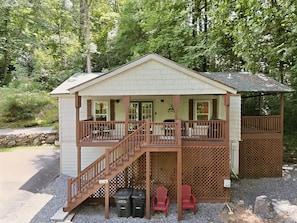 A two-story cabin with a balcony, a covered porch, and a stone wall.