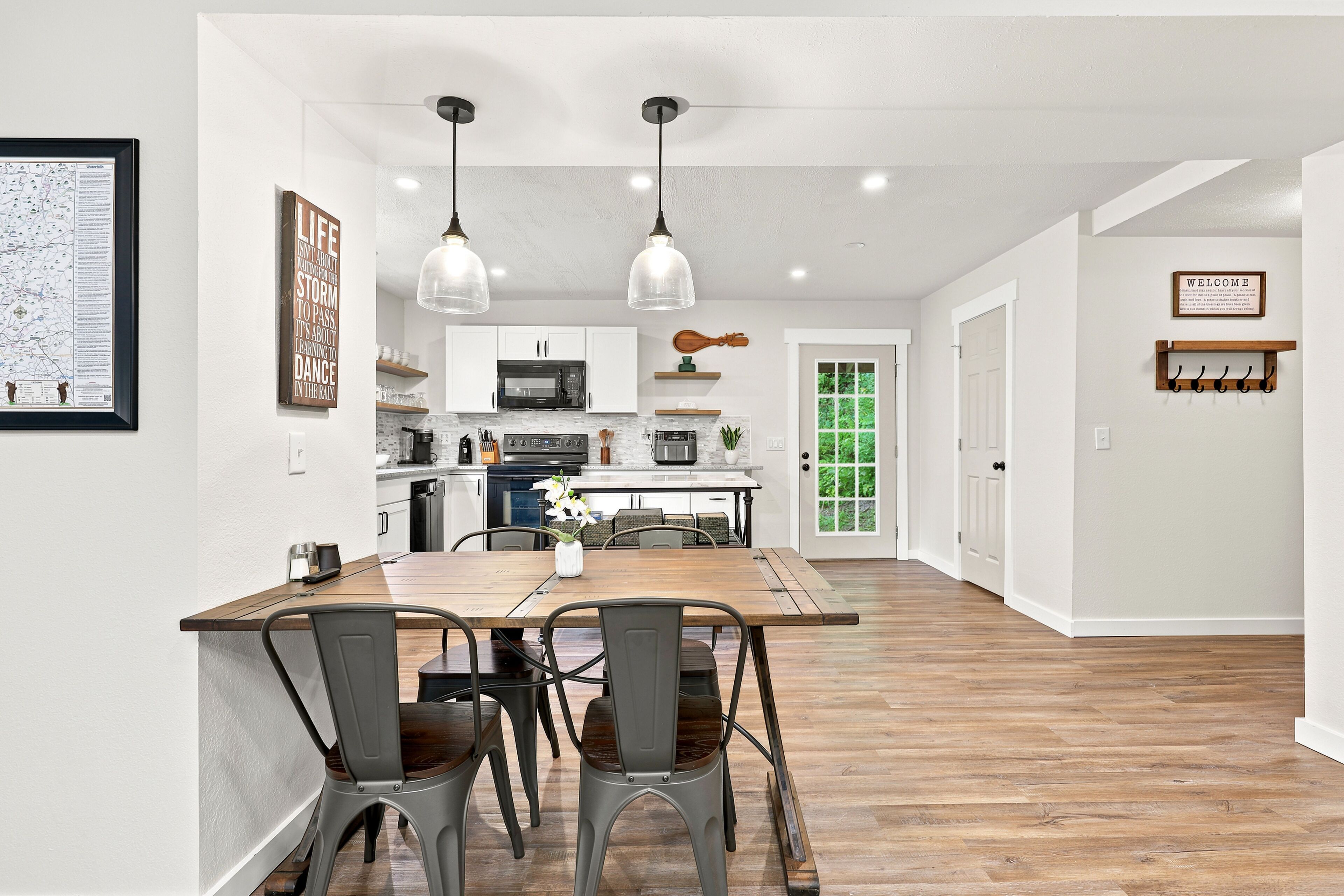 A modern kitchen with white cabinets, a wooden dining table, and two pendant lights.