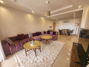 A modern living room with a sectional sofa, two round coffee tables, and a dining area with a table and chairs. - Cozy apartment in the heart of Marrakech with a pool (Marrakech)
