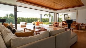 A modern living room with a large sofa, a coffee table, and a dining area with chairs and a table.