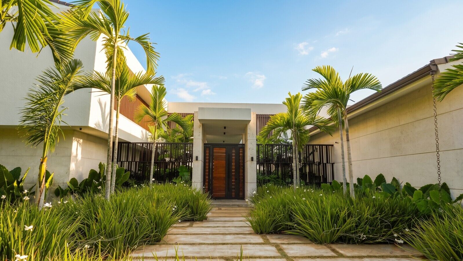 Uma casa moderna com entrada central, cercada por vegetação exuberante e palmeiras.