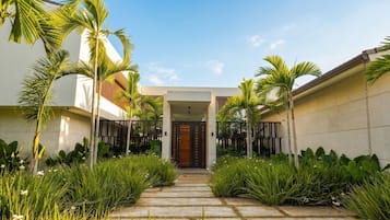 A modern house with a central entrance, surrounded by lush greenery and palm trees.