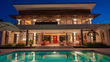 A modern two-story house with a swimming pool, outdoor seating, and a well-lit entrance.