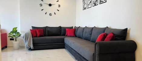 A living room with a sectional sofa, a wall clock, and framed artwork.