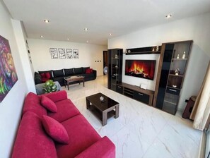 Ein modernes Wohnzimmer mit einem roten Sofa, einem Couchtisch, einem Kamin und einem an der Wand befestigten Fernseher.